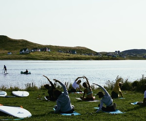 Un groupe pratique une activité de yoga guidée offerte par Cindy Hook aux iles de la madeleine dans un paysage d'Hâvre aux maison.